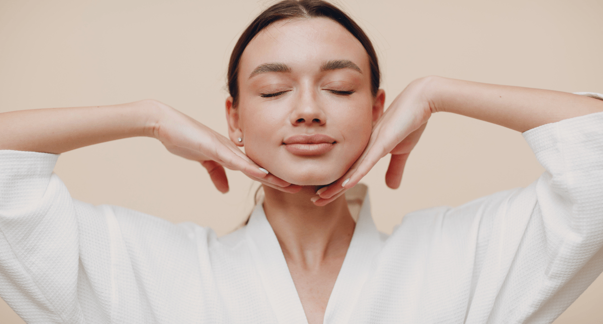 Woman with clear skin in white robe gently touching chin, showcasing skincare results