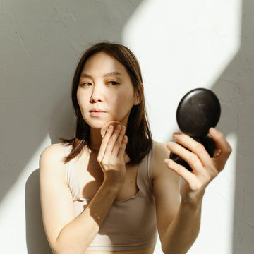 Woman checking her makeup in a compact mirror while applying foundation with a sponge