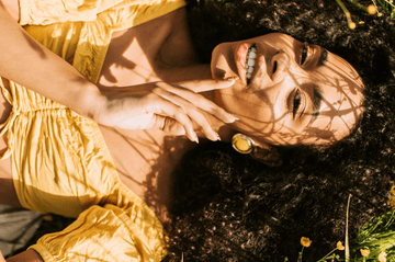 Woman in a yellow dress touching her cheek outdoors in dappled sunlight