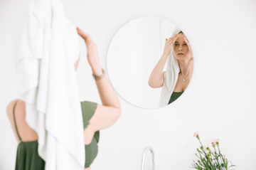 Woman touches her face in a bathroom mirror with a towel wrapped around her head