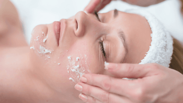 Person receiving a facial treatment with white exfoliating product applied to the cheek