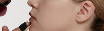 Close-up of a person applying makeup to their chin with a black finger makeup applicator against a white background