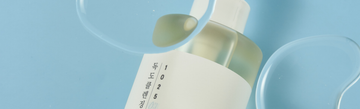 Oil cleanser bottle beside a glass spoon and dish on a blue background