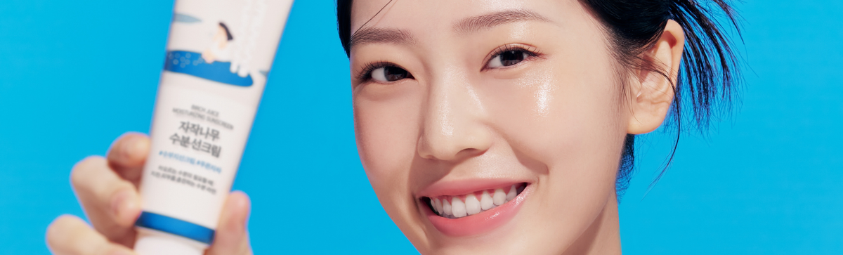 Woman holding a Birch sunscreen tube against a bright blue background