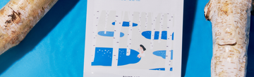 Birch logs frame an illustration of a woman beside blue water on a bright blue background