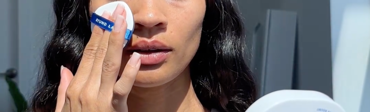 Woman reapplying sunscreen over makeup with a cushion puff in bright natural light