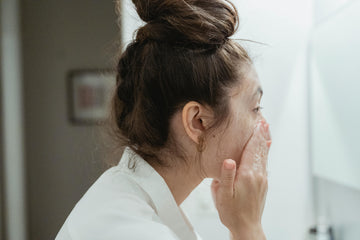 Woman cleansing her face with her hands in a bright bathroom