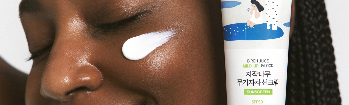 Person with sunscreen applied to cheek beside a sunscreen tube in close-up