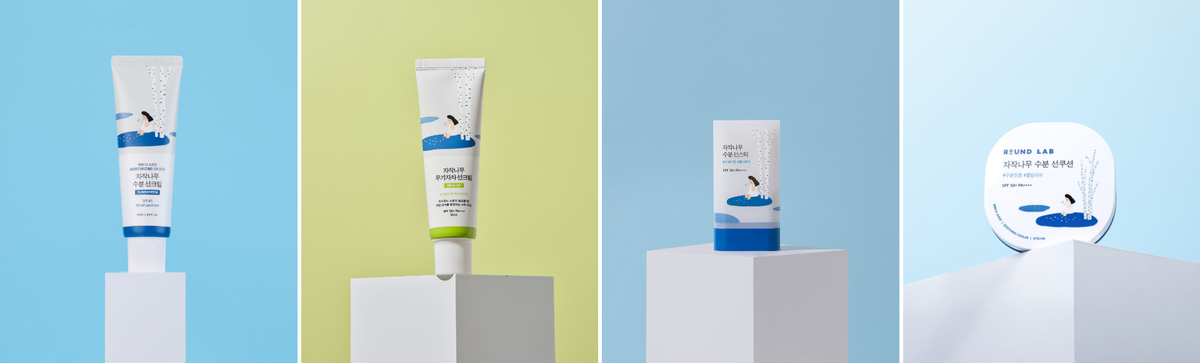 Front view of Round Lab sunscreens showcasing tube and compact packaging on white pedestals against blue and green backgrounds