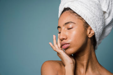 Woman touching her face while wearing a towel head wrap against a blue background