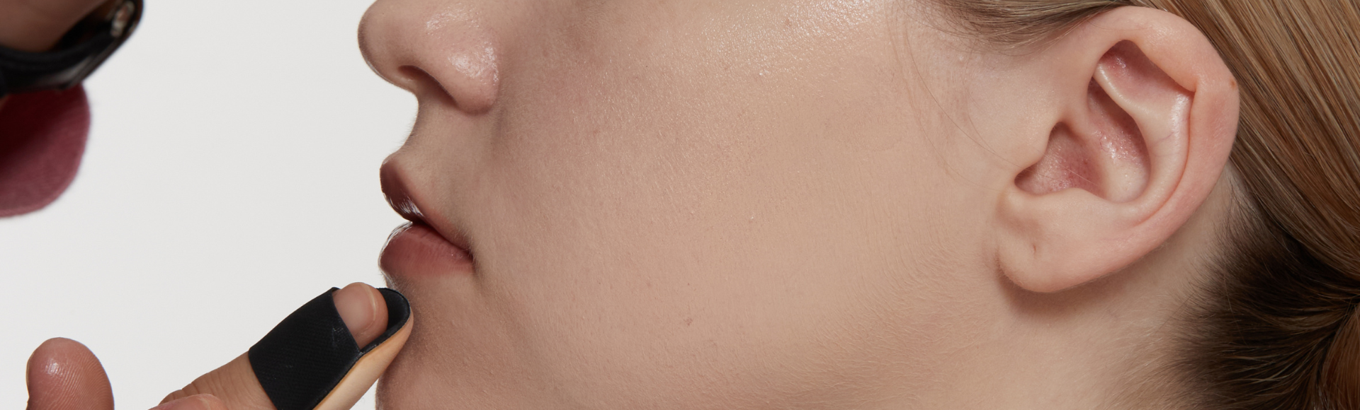 Close-up of makeup artist applying natural nude lipstick to a woman's lips, highlighting smooth, radiant skin.