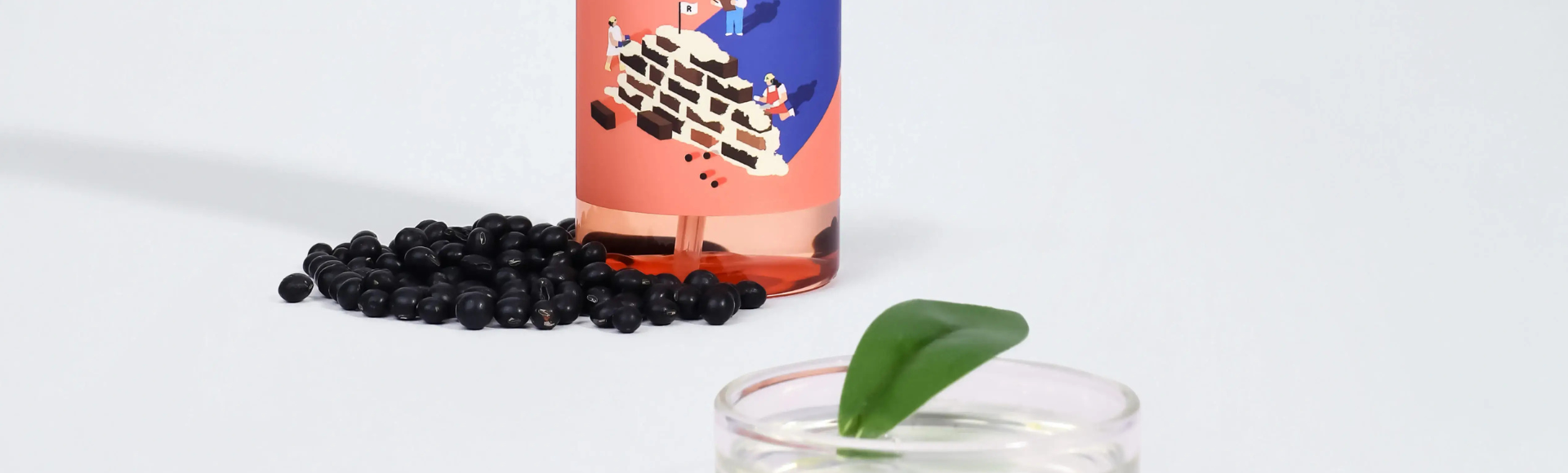 Skincare product bottle with illustrated label, black beans, and glass of water with leaf