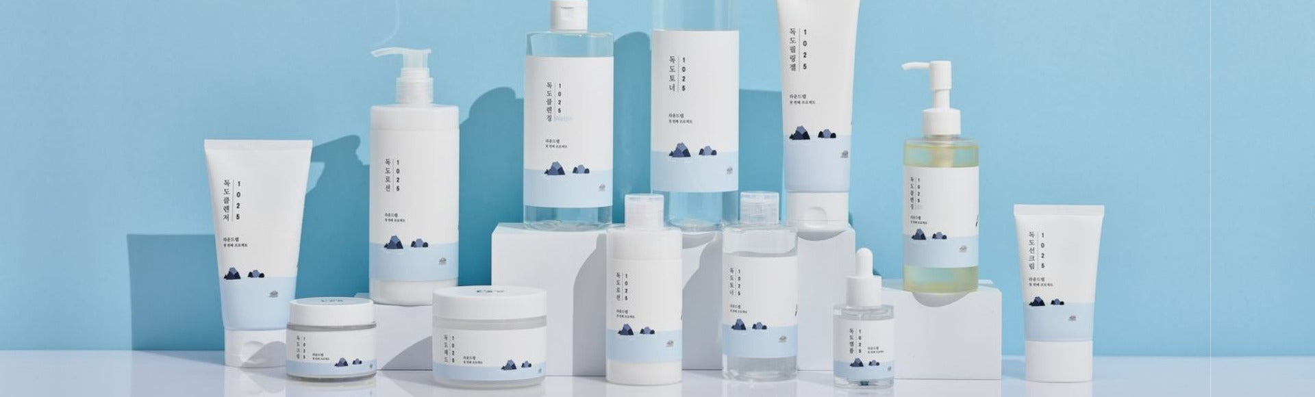 Clean Korean skincare products arranged on white blocks with minimalist blue packaging