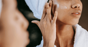 Woman applying face cream in bathroom, skincare routine, towel on head, healthy glowing skin