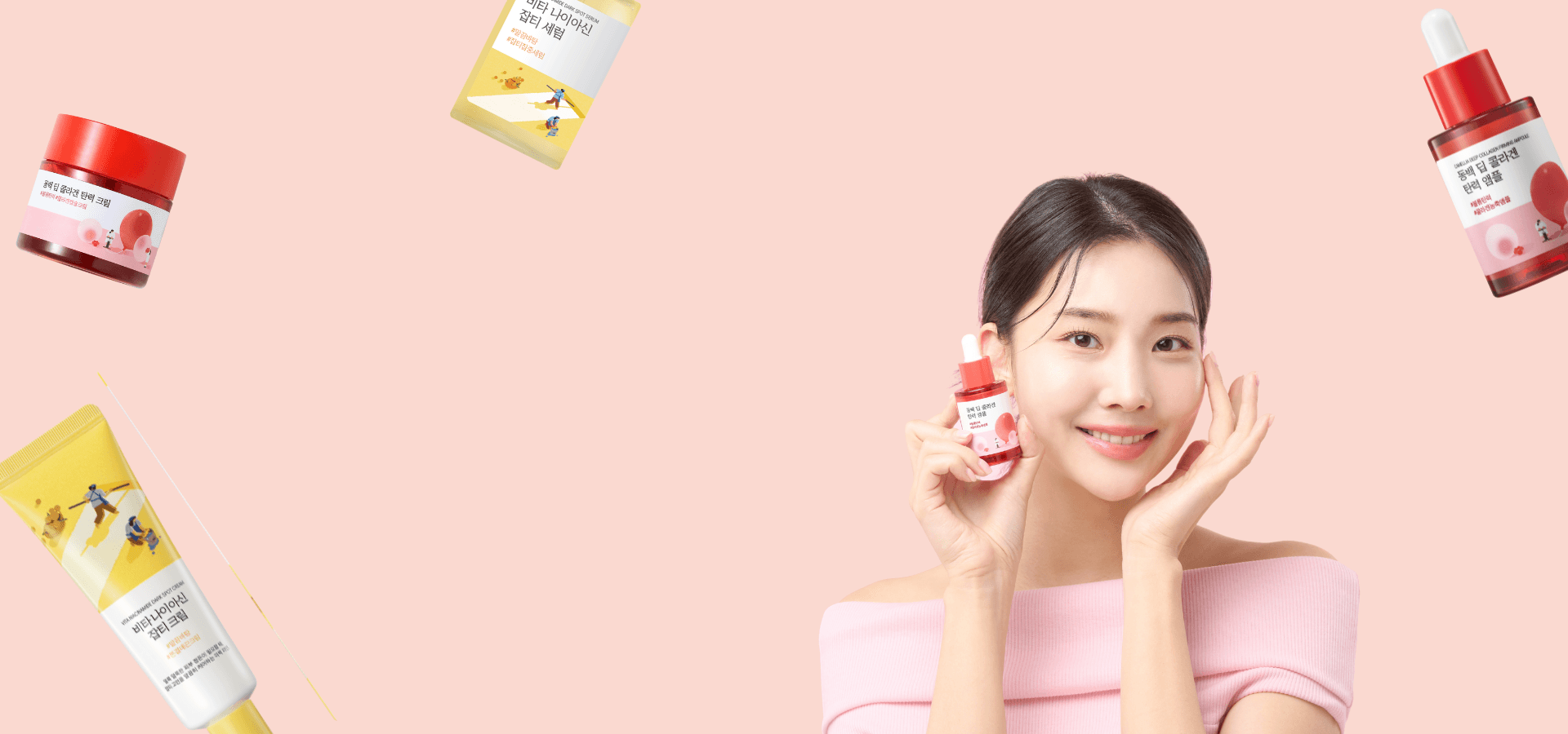 Smiling woman holding skincare serum with various K-beauty products on a pink background