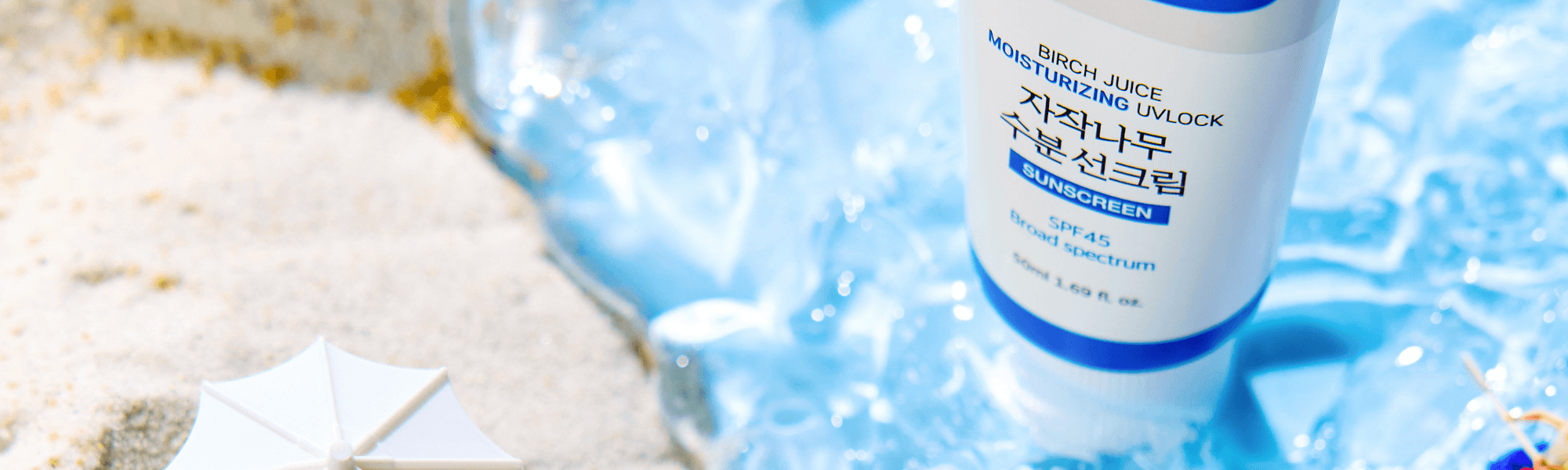 Moisturizing birch juice sunscreen SPF 45 on sand with blue ice and a small umbrella, summer skincare.