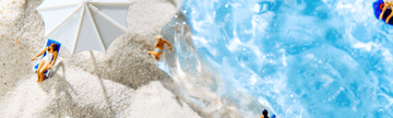 Miniature beach scene with figures relaxing on sand under umbrella, blue water nearby