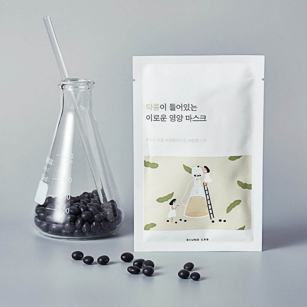 Front view of Soybean Nourishing Sheet Mask pouch and box beside black soybeans on a wooden tray